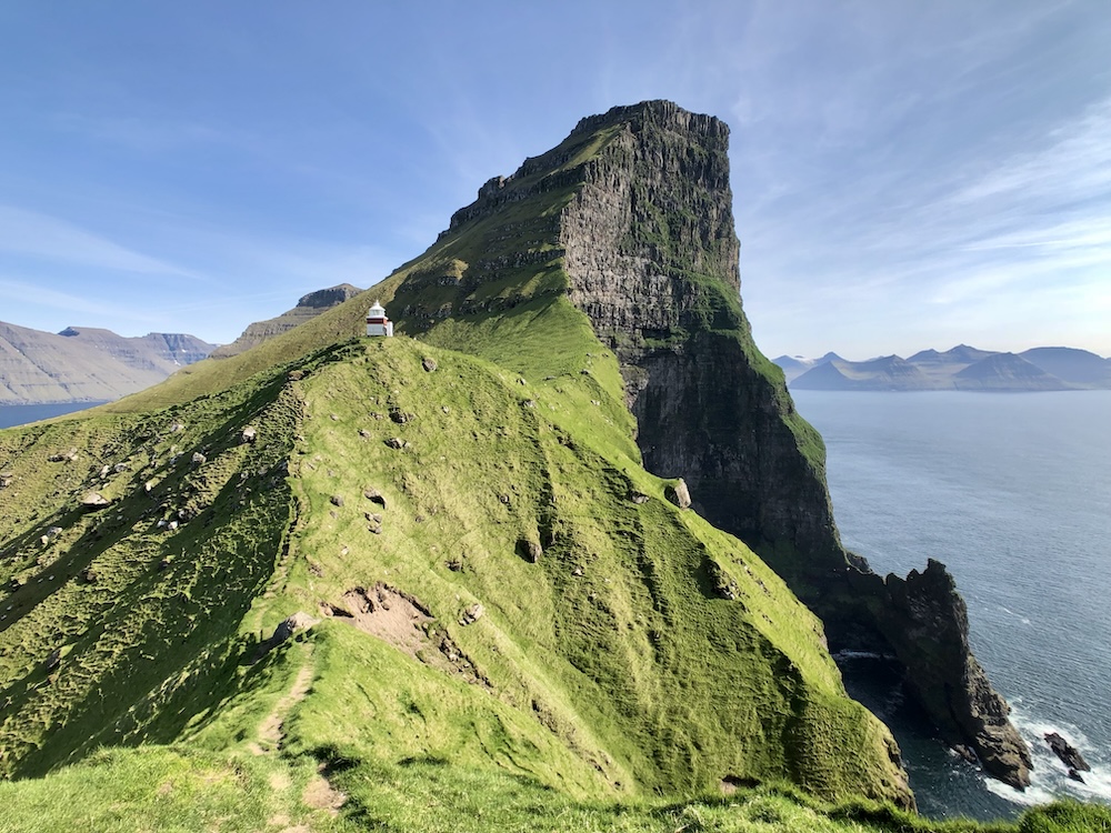 Grassy ridge with a small white–red lighthouse above sea cliffs